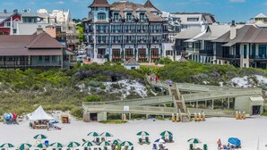 A beachfront hotel with a prominent tower, a wooden boardwalk leading to the beach, and numerous beach umbrellas. - Rollin Tide Villas- Rollin Tide B9 (Santa Rosa Beach)