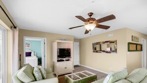 A living room with a ceiling fan, a television on a cabinet, and a coffee table. - Rollin Tide Villas- Rollin Tide B9 (Santa Rosa Beach)