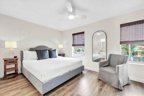 A bedroom with a bed, bedside tables, a chair, a ceiling fan, and windows with blinds. - Palm Grove at Sago Sands Unit A (Santa Rosa Beach)