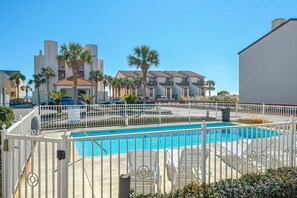 A swimming pool with a white fence, palm trees, and a building with multiple balconies in the background. - Palm Grove at Sago Sands Unit A (Santa Rosa Beach)