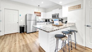A modern kitchen with white cabinetry, stainless steel appliances, a marble countertop, and a bar stool area. - Palm Grove at Sago Sands Unit A (Santa Rosa Beach)