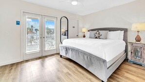 A bedroom with a bed, two bedside lamps, a ceiling fan, and a large mirror. - Palm Grove at Sago Sands Unit A (Santa Rosa Beach)