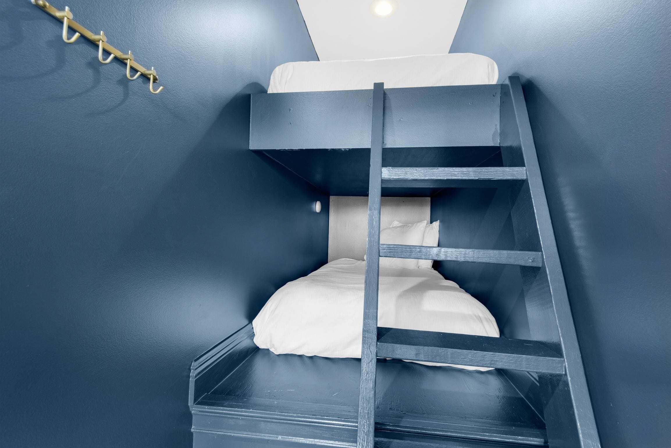 Un lit superposé avec une échelle, du linge de lit blanc et un crochet au mur.