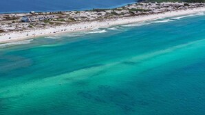 Eine Luftaufnahme eines Strandes mit klarem türkisblauem Wasser, einem sandigen Ufer und einem kleinen Gebäude mit blauem Dach.