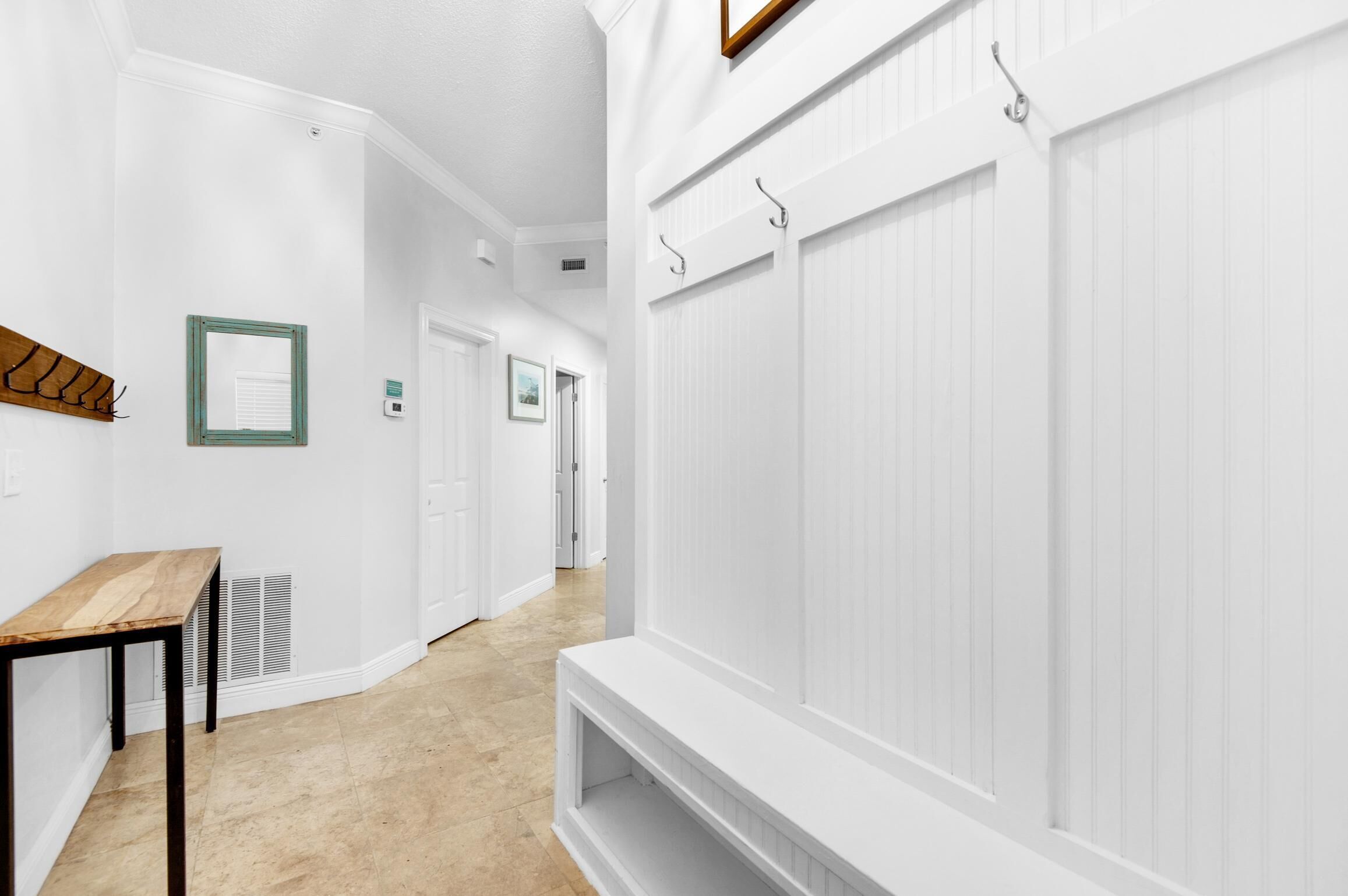 A hallway with white walls, a wooden bench, a vent, and a door at the end.