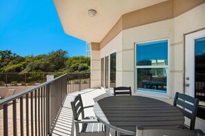 A balcony with a table and chairs, a glass door, and a view of trees and buildings. - Legacy 104 (Santa Rosa Beach)