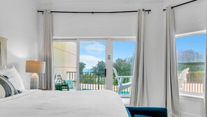 A hotel room with a large bed, a bedside lamp, a view of a pool and outdoor seating. - Legacy 104 (Santa Rosa Beach)