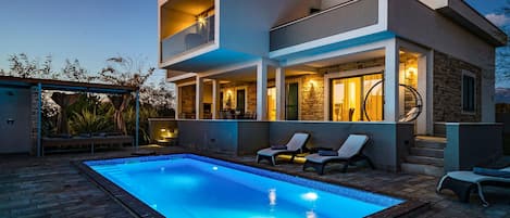 A modern two-story house with a swimming pool, outdoor seating, and a stone facade.