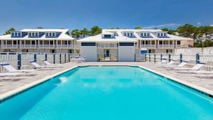 Et poolområde med et klart blåt pool, liggestole og en bygning med flere altaner.