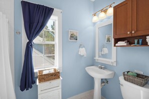 A bathroom with a white sink, a wooden cabinet, a window with a blue curtain, and a wall-mounted light fixture.