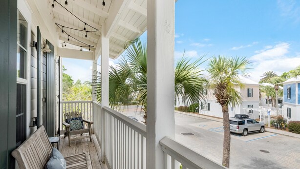 A covered porch with a bench and a chair, overlooking a street with parked cars and palm trees. - Four Fish Bungalow 155 (Santa Rosa Beach)