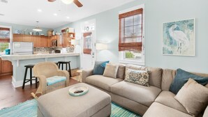 A living room with a beige sofa, a wooden ceiling fan, and a kitchen in the background. - Four Fish Bungalow 155 (Santa Rosa Beach)