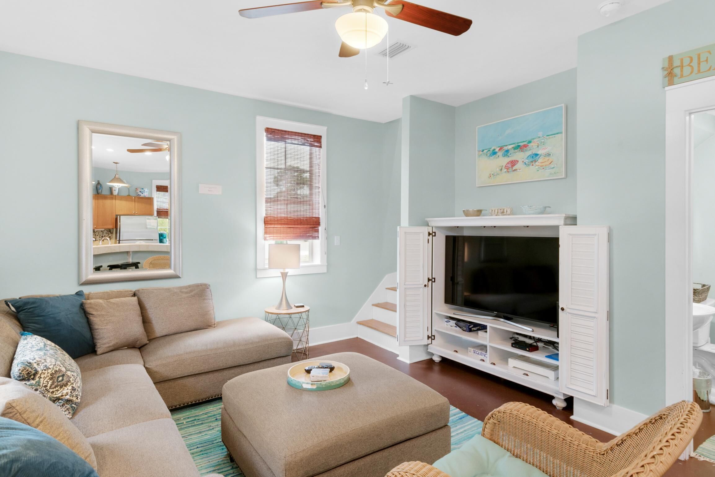 A living room with a sectional sofa, ottoman, TV stand, and wicker chair.