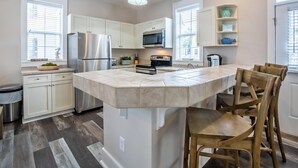 A modern kitchen with white cabinets, stainless steel appliances, and a large island with bar stools. - Coastal Blue 141 (Santa Rosa Beach)