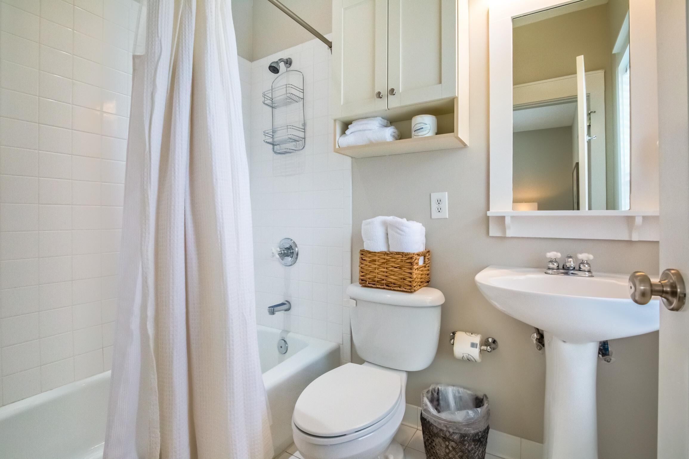 A bathroom with a toilet, a sink, a shower curtain, a bathtub, and a mirror.