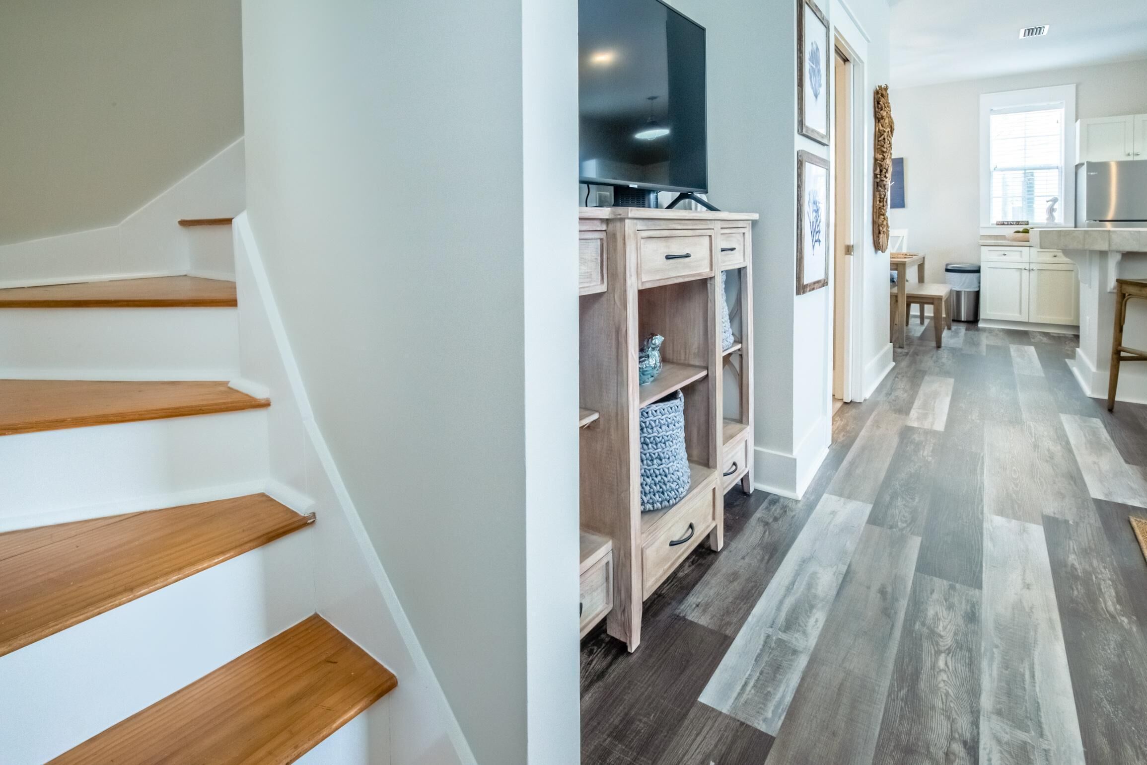 A staircase with wooden steps leading to a living area with a TV, wooden shelving, and a kitchen area with a window.
