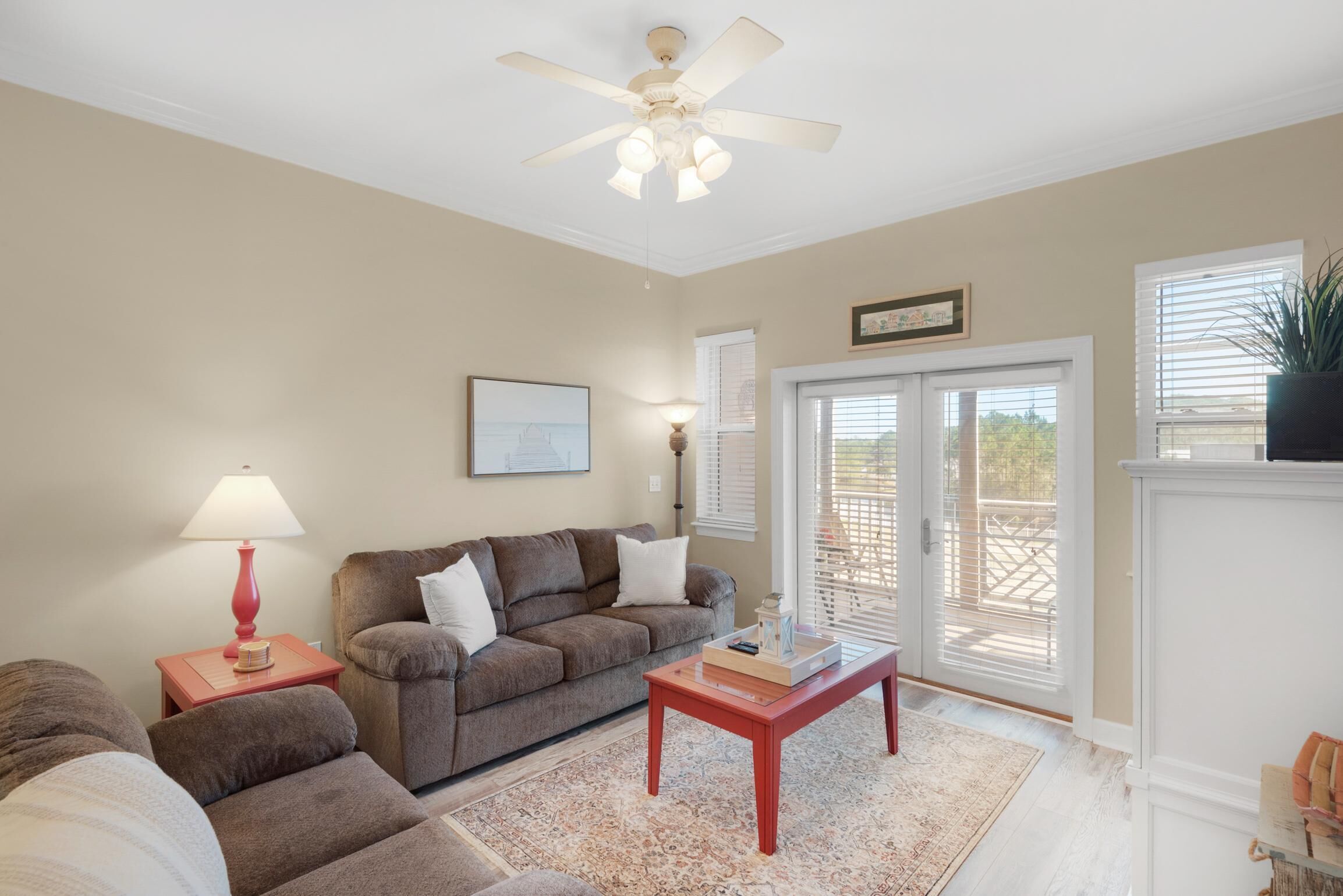 A living room with a brown sofa, a red coffee table, a ceiling fan, and a large window with blinds.