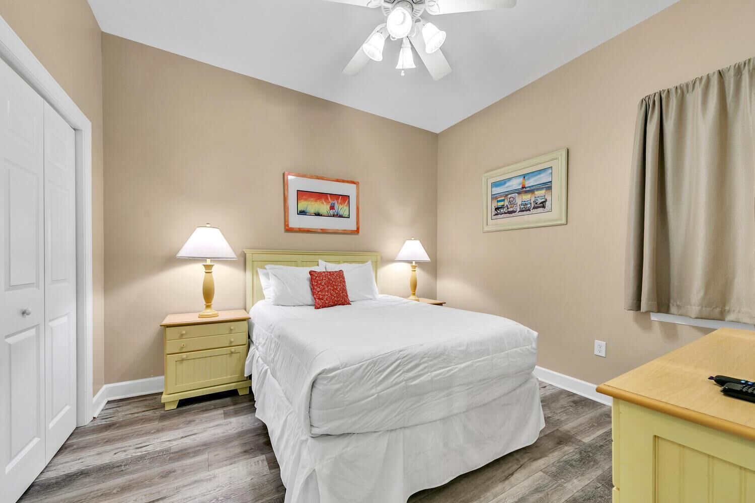 A bedroom with a bed, two bedside tables, a ceiling fan, and two framed pictures on the wall.