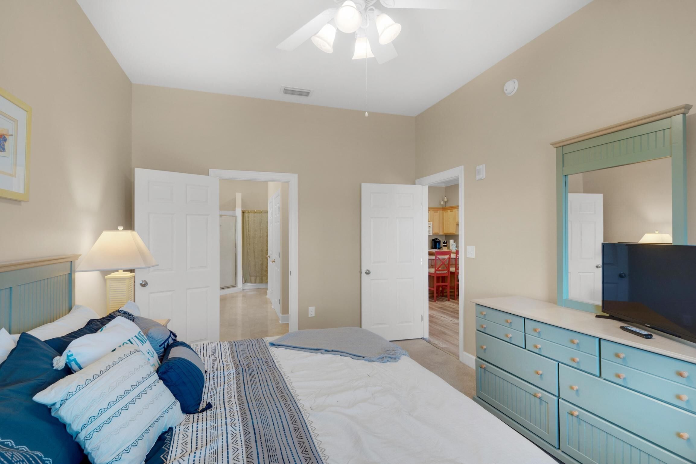 A bedroom with a bed, dresser, TV, and a ceiling fan.