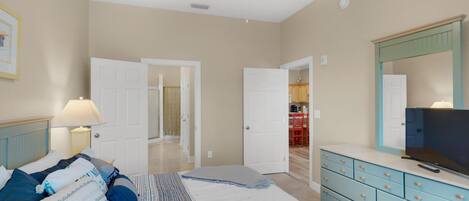 A bedroom with a bed, dresser, TV, and a ceiling fan.