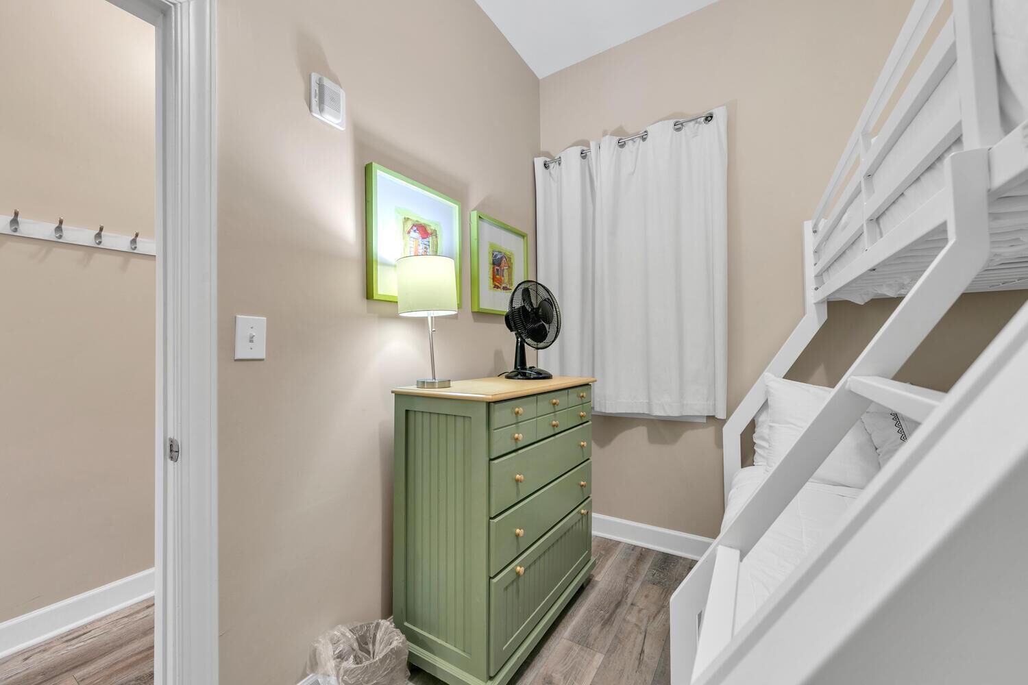 A hallway with a green dresser, a fan, and a white staircase.