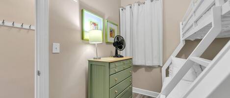 A hallway with a green dresser, a fan, and a white staircase.
