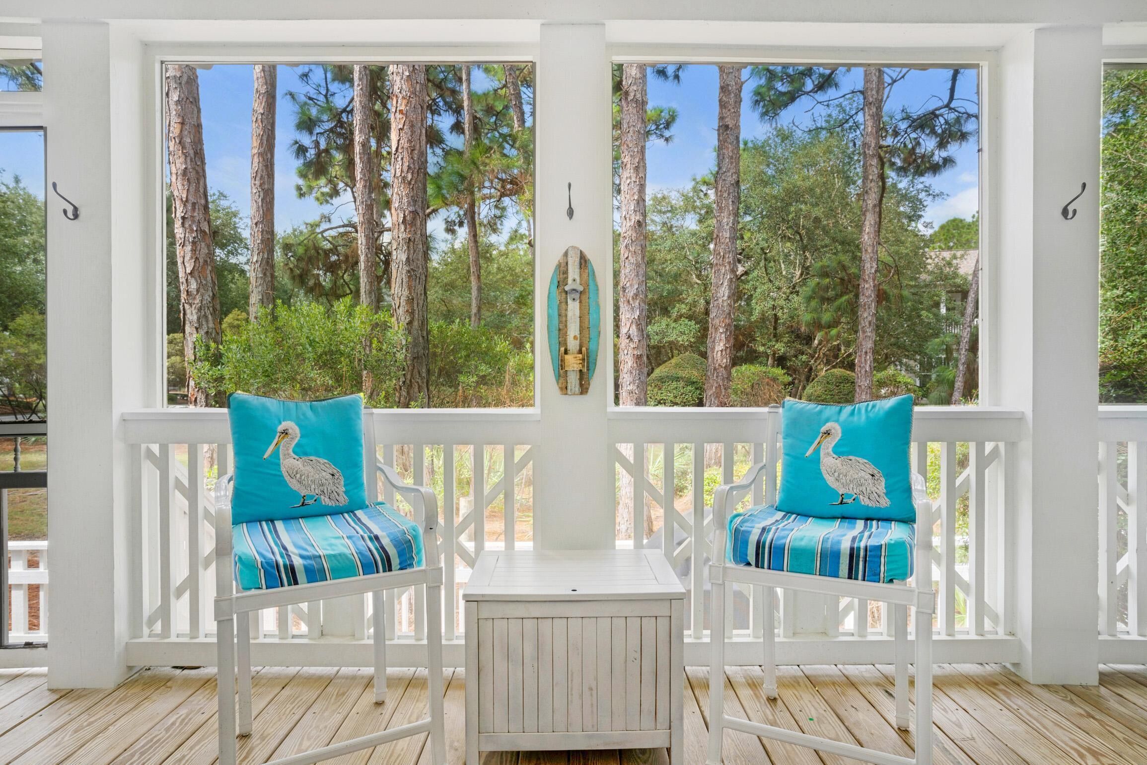A covered porch with two white chairs, each with a teal cushion featuring a pelican design.