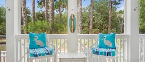A covered porch with two white chairs, each with a teal cushion featuring a pelican design.