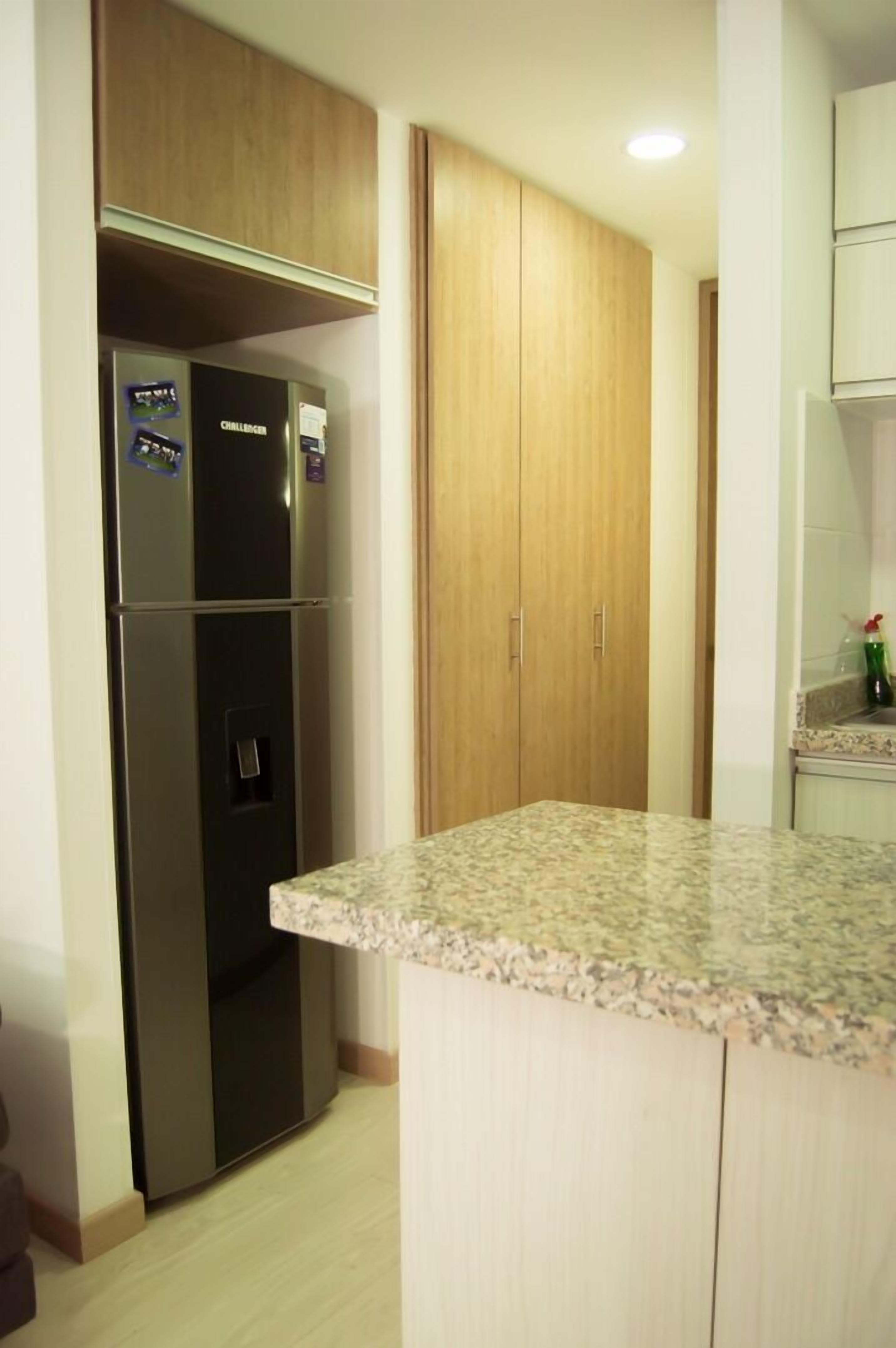 A kitchen with a stainless steel refrigerator, wooden cabinets, and a granite countertop.
