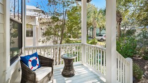 A covered porch with wicker furniture, a glass table, and a view of the neighborhood. - Calm Breeze Cottage (Santa Rosa Beach)