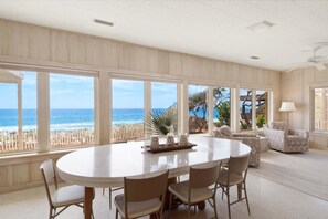A spacious room with a large dining table and chairs, a sofa, and a chair, with a view of the ocean through large windows. - Butterfly Bluff (Santa Rosa Beach)
