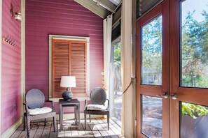 A porch with two wicker chairs, a small table with a lamp, and a wooden door. - Bramble Cottage (Santa Rosa Beach)