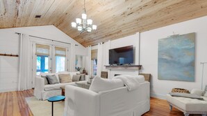 A spacious living room with a white sofa, a television, and a painting on the wall. - Bramble Cottage (Santa Rosa Beach)