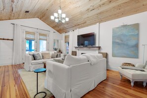 A spacious living room with a white sofa, a television, and a painting on the wall. - Bramble Cottage (Santa Rosa Beach)