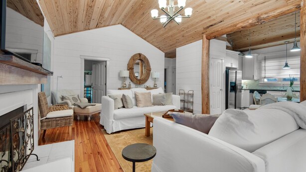 A spacious living room with a white sofa, a coffee table, and a fireplace. There is a wooden ceiling and a chandelier. - Bramble Cottage (Santa Rosa Beach)