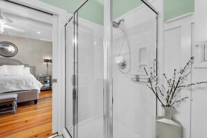 Relax in a clean, minimalist space with a glass-enclosed shower, a comfortable bed, and a bedside table with a lamp.