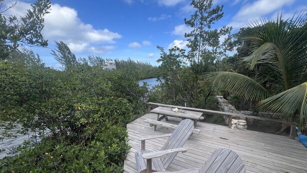 Een houten terras met een tafel en stoelen, omgeven door weelderige begroeiing en uitzicht op een waterpartij.