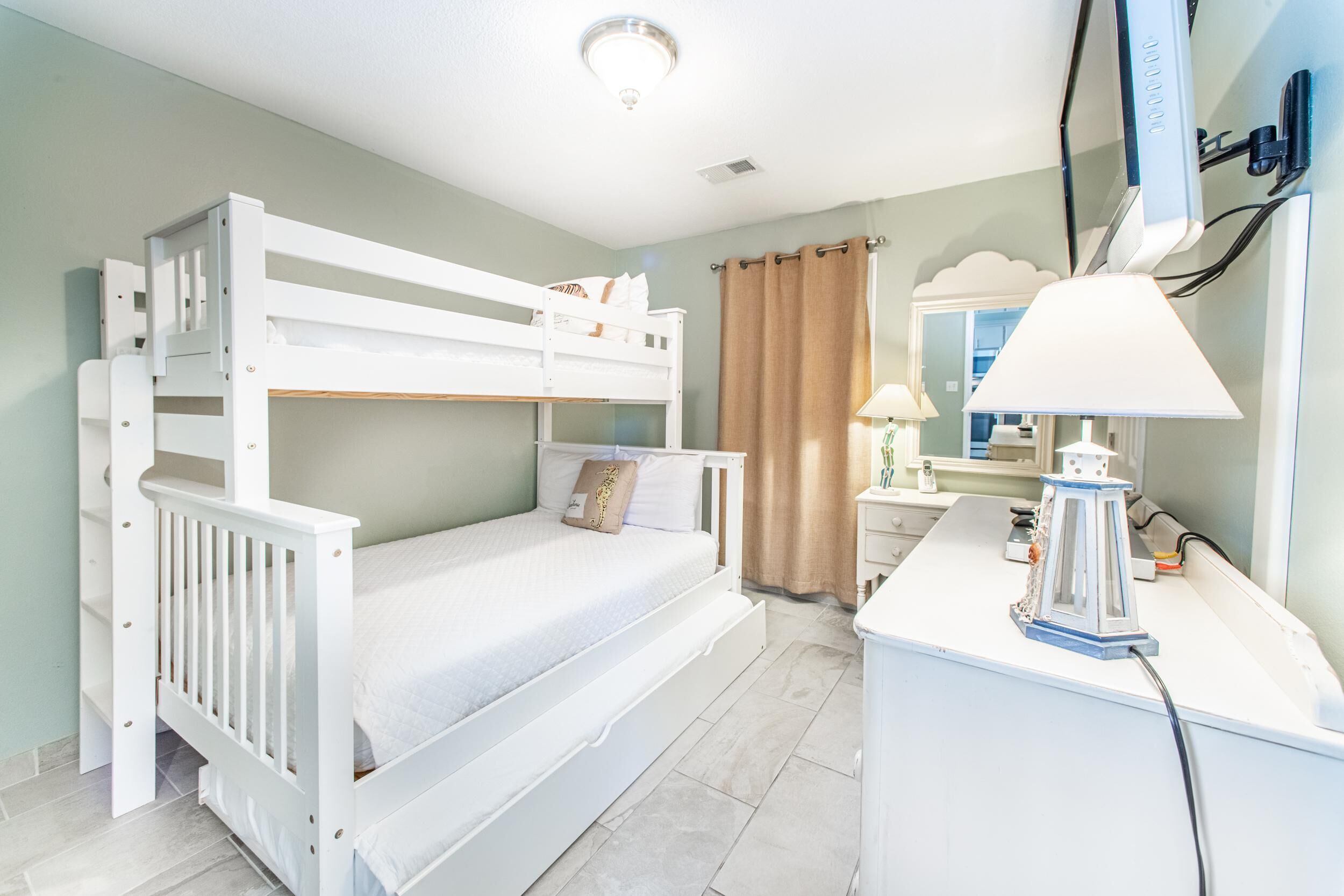 A bunk bed room with a desk and lamp, a mirror, and a curtain.