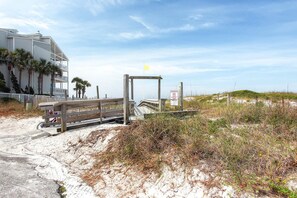 A beachside building with a wooden deck, a flag, and a sign indicating a beach access point. - Beachside Villas 332 (Santa Rosa Beach)