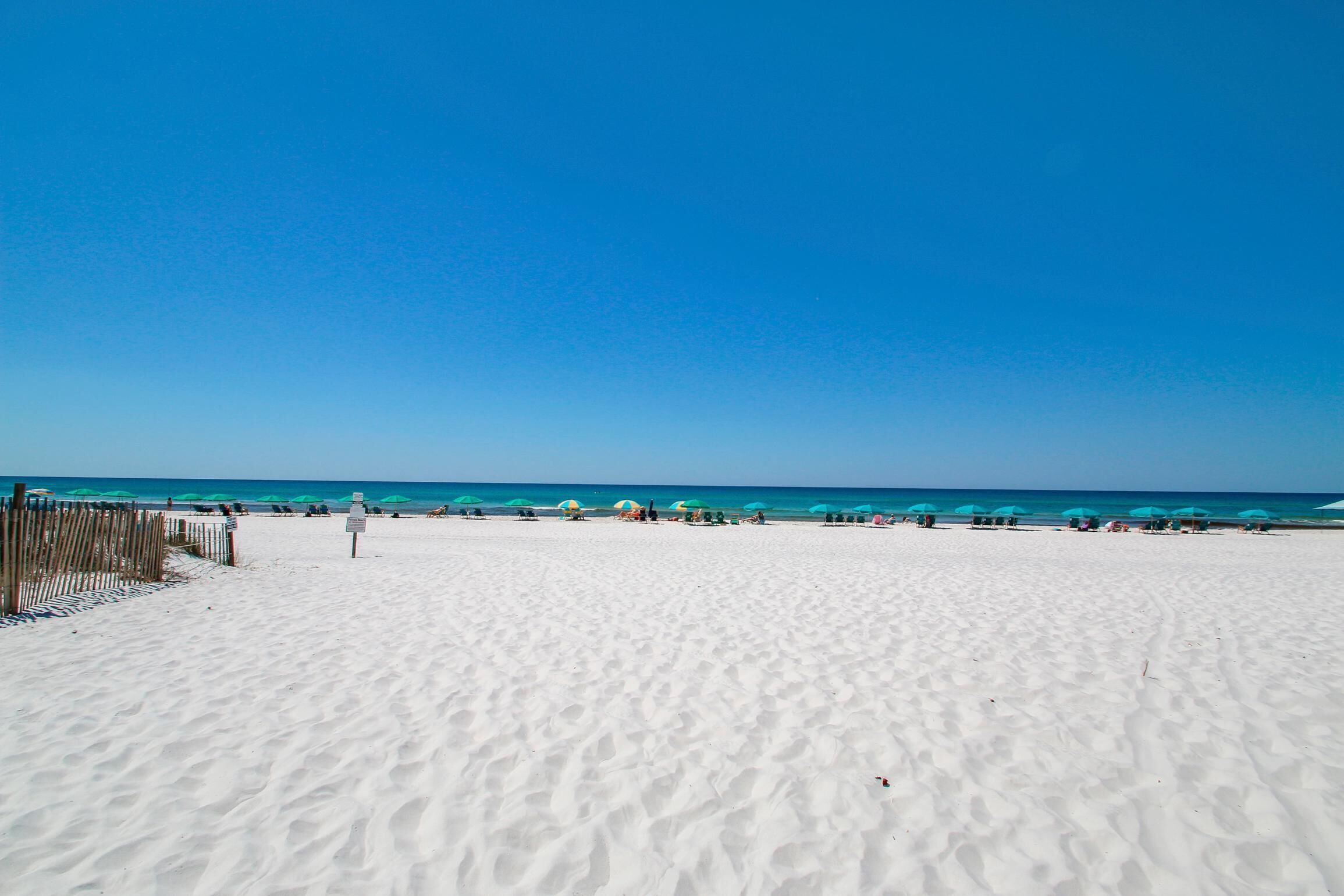 Ampia spiaggia sabbiosa con una recinzione di legno sul lato sinistro e diversi ombrelloni in lontananza.