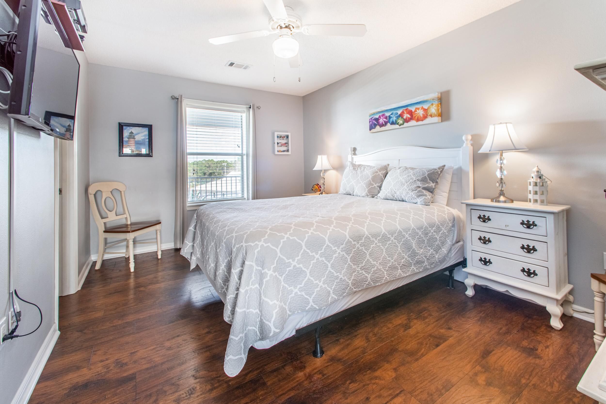 A bedroom with a bed, a nightstand, a chair, a ceiling fan, and a window with blinds.