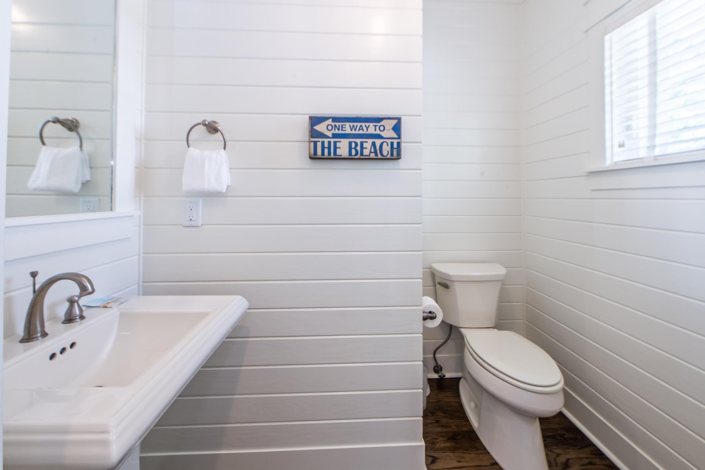 A bathroom with a white sink, toilet, and a sign that reads "ONE WAY TO THE BEACH".