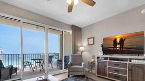 A living room with a large window overlooking the ocean, a flat-screen TV, a comfortable armchair, and a small table with decorative items. - Ariel Dunes I 1505 (Miramar Beach)