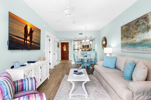 A living room with a sofa, chairs, a coffee table, a TV, and artwork on the walls. - Pilot House 506 (Miramar Beach)