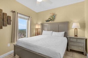 A bedroom with a bed, nightstands, a ceiling fan, a window with curtains, and a decorative wall piece. - Splash 1803e (Panama City Beach)