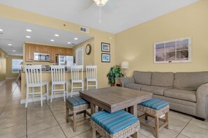 A spacious living area with a wooden dining table, white chairs, and a beige sofa. - Splash 1803e (Panama City Beach)