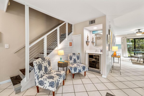 A living room with a staircase, two patterned chairs, a fireplace, and a dining area with outdoor seating.