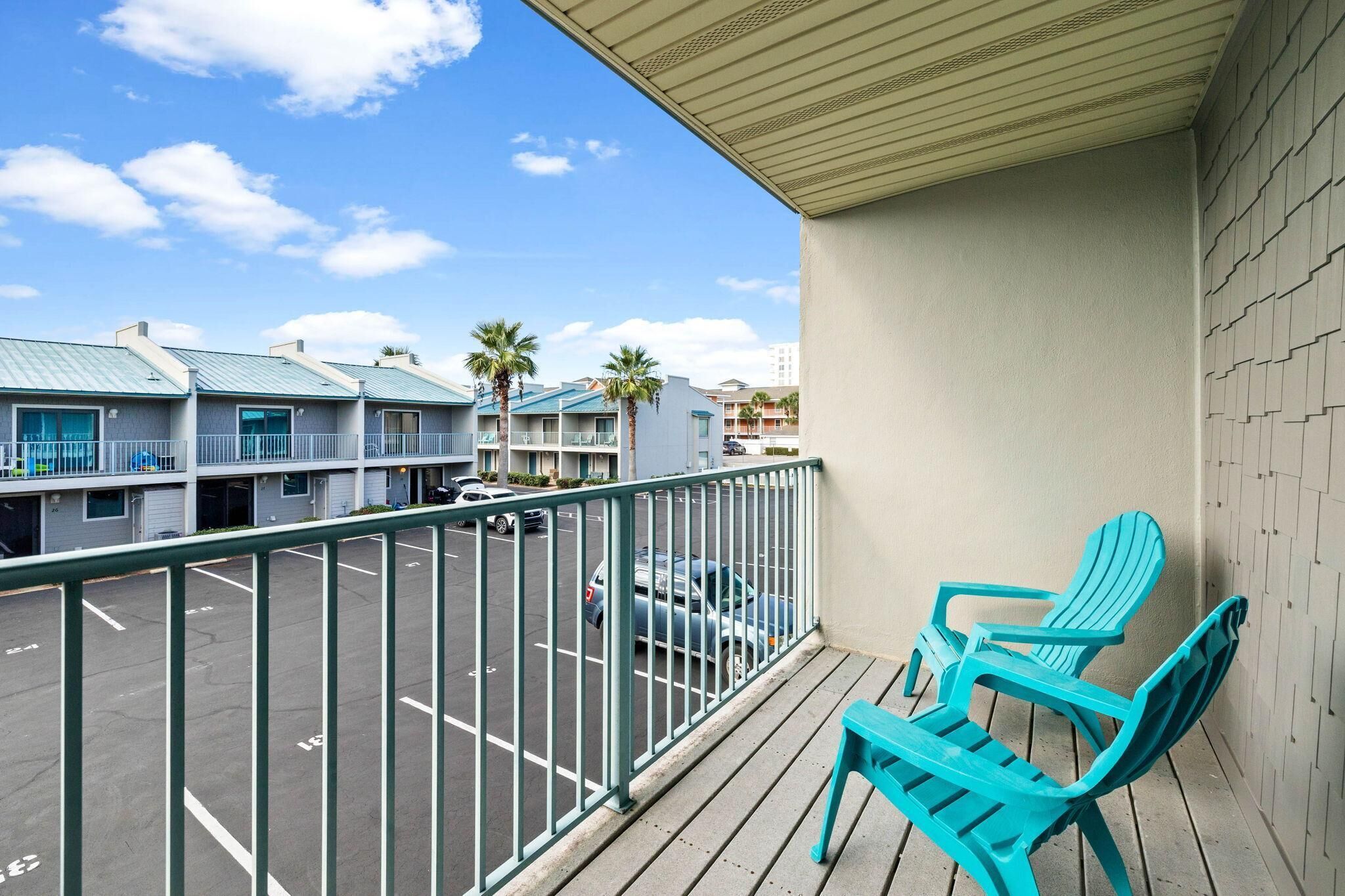 A balcony with turquoise chairs, a view of a parking lot, and buildings with blue roofs.