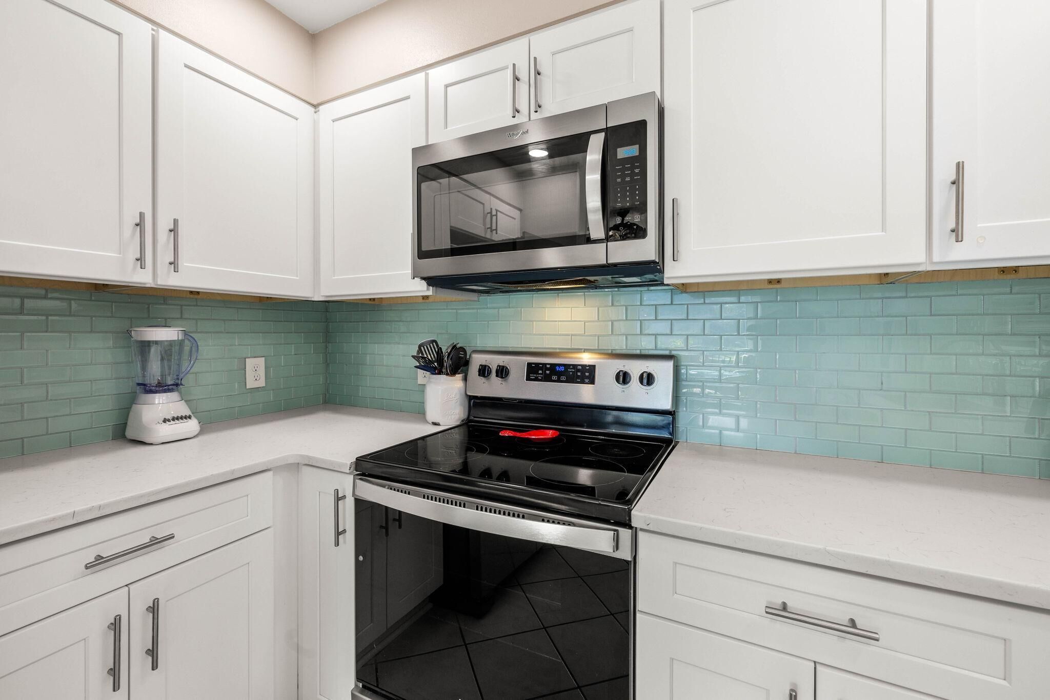 A kitchen with white cabinets, a stainless steel microwave, a gas stove, and a blender on the counter.