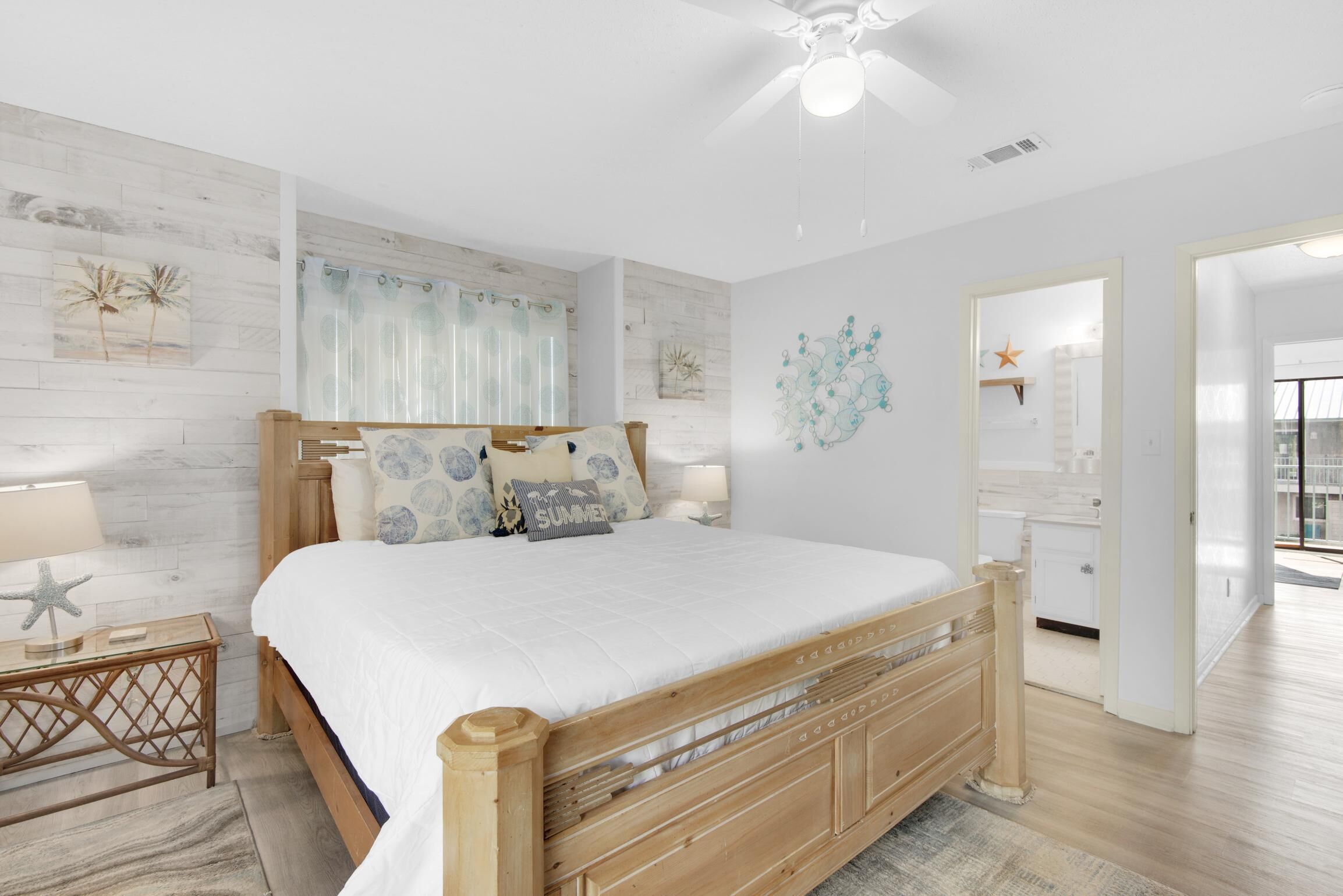A bedroom with a wooden bed, white bedding, a nightstand with a lamp, a starfish decoration, and a wall with a tropical mural.